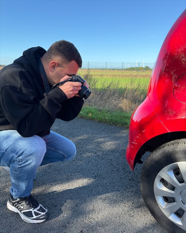 Phillip Manthey fotografiert einen Unfallschaden am Heck eines roten Autos
